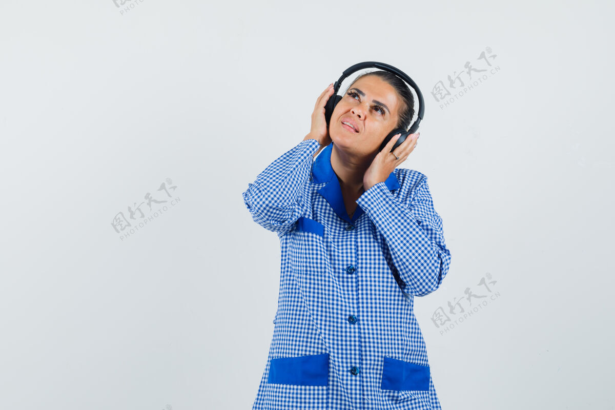 干净穿着蓝色方格布睡衣衬衫的年轻女子戴着耳机听音乐 抬头看去 看上去很漂亮 正前方自然女孩漂亮