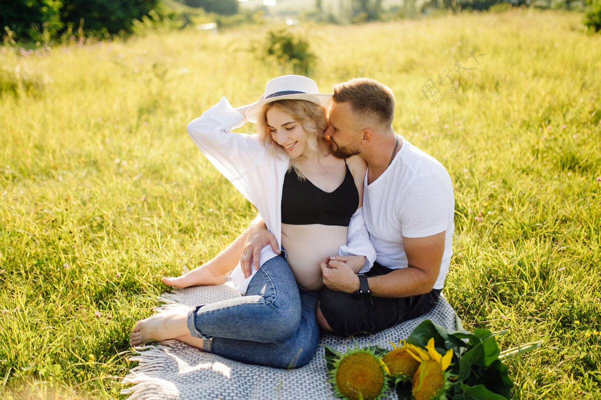 腹部年轻的孕妇和她的男人在公园户外放松成人期望女性