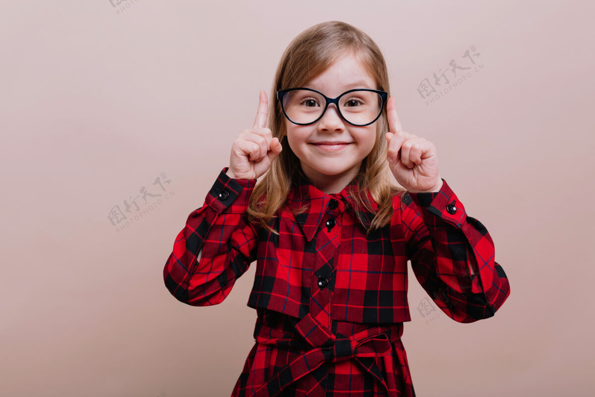 表情漂亮聪明的小女孩站在米色的墙上 微笑着举起大手指享受惊喜情感