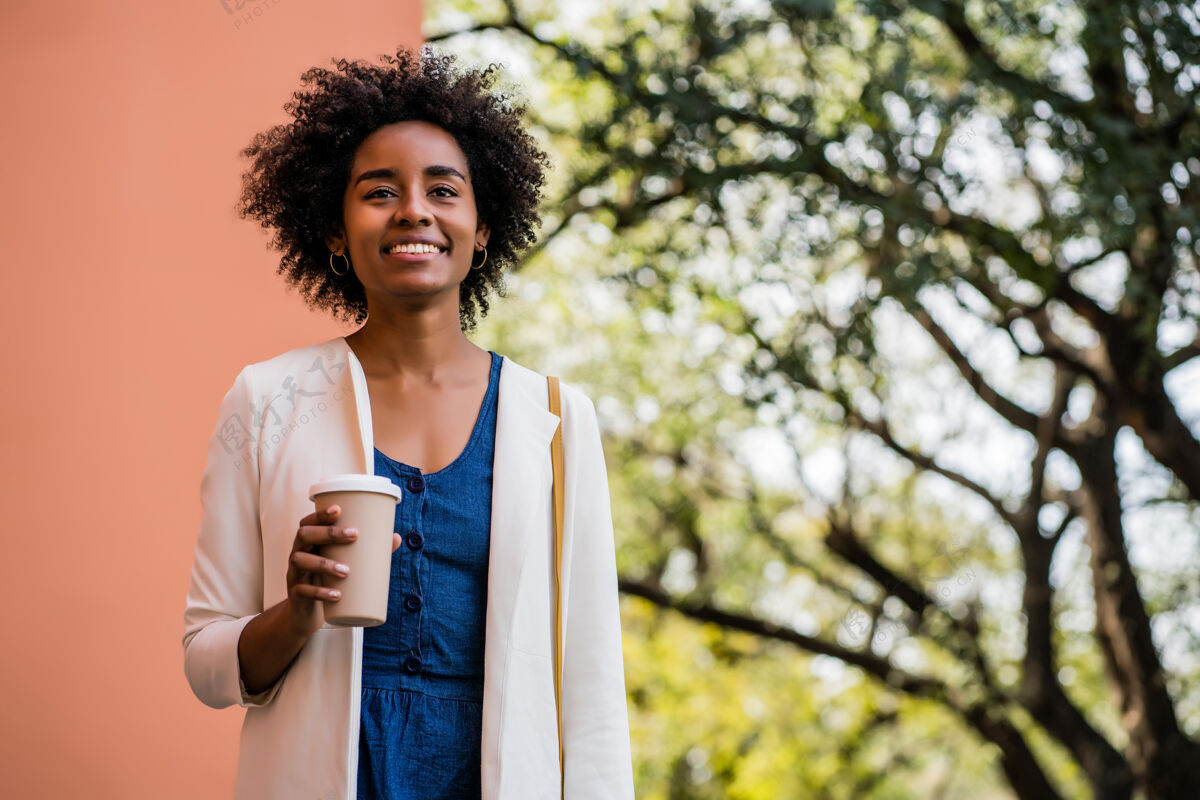 年轻一幅非洲女商人微笑着拿着一杯咖啡站在街上的照片商业和城市概念微笑专业人士站立