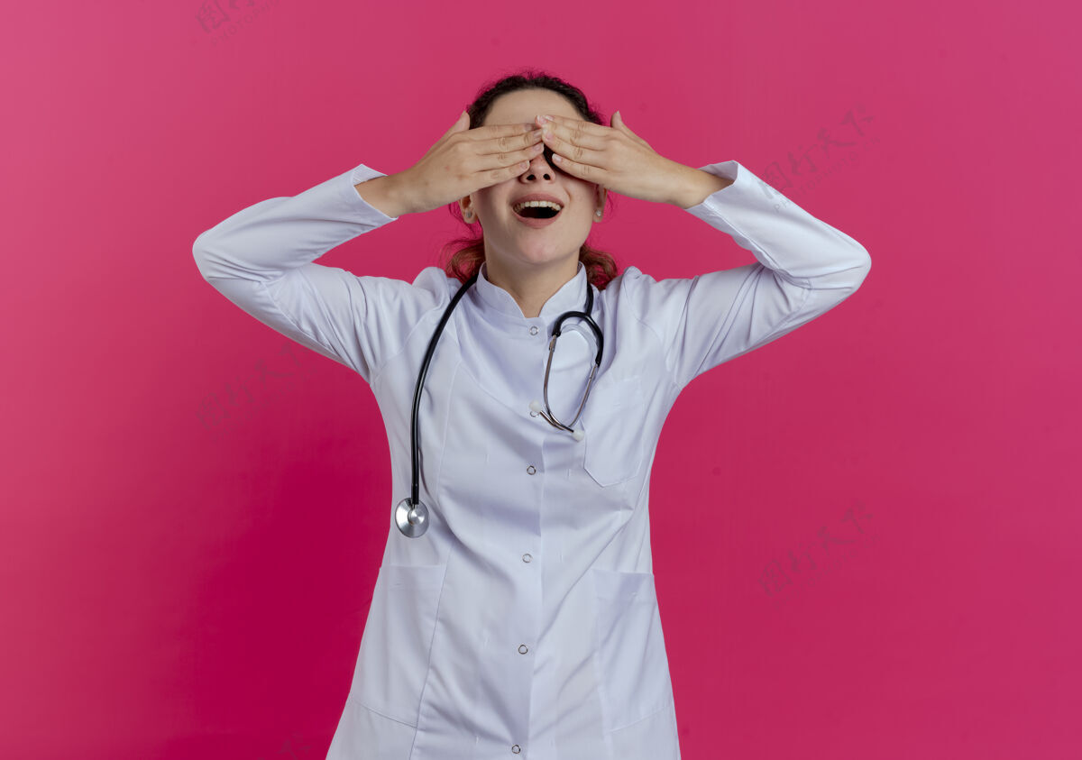 手年轻的女医生穿着医用长袍 戴着听诊器 戴着眼镜 手被隔离在粉红色的墙上穿盖女