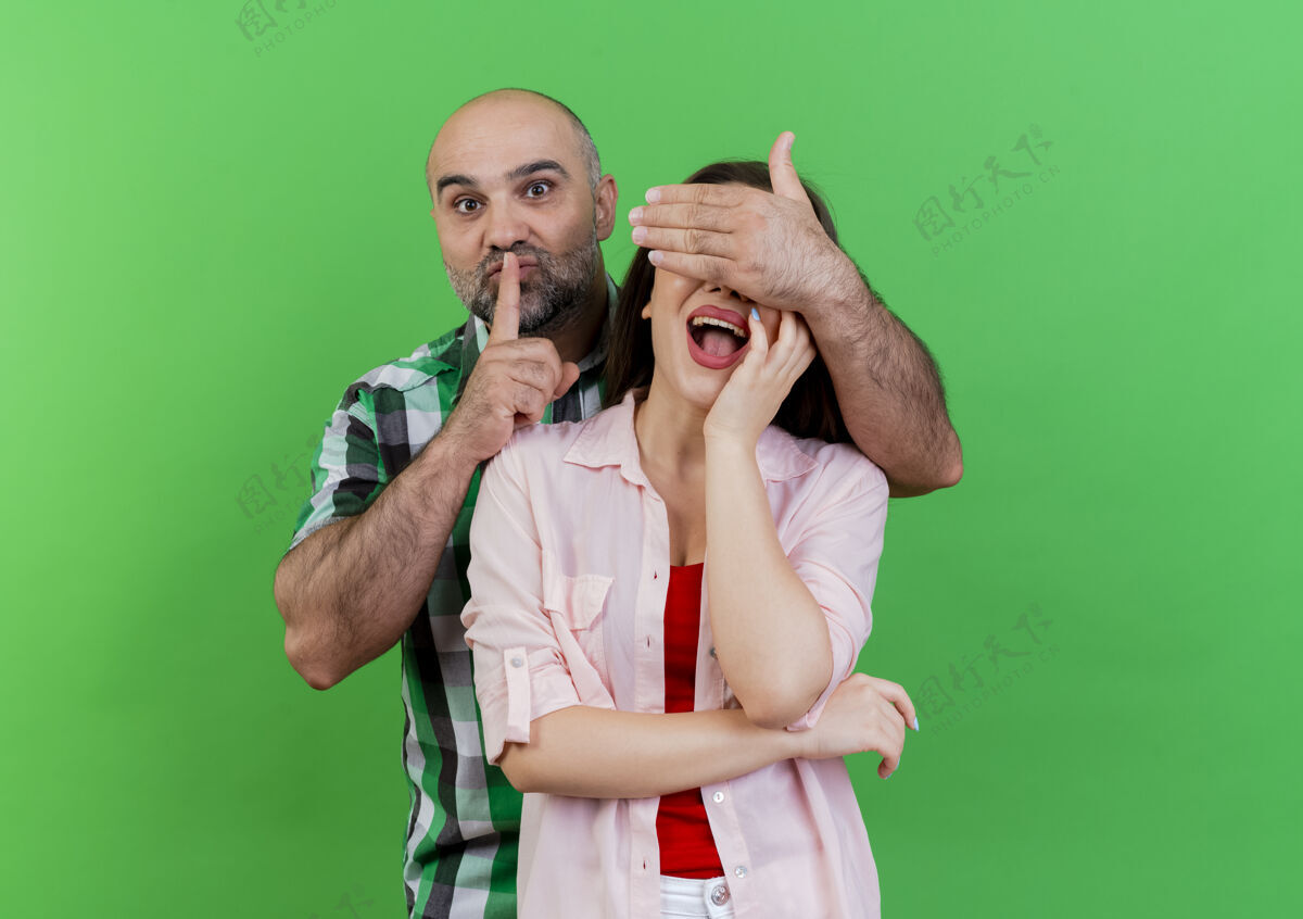 印象令人印象深刻的成年夫妇男人用手捂住女人的眼睛示意沉默女人把手放在脸上隔离在绿色的墙壁上复制空间沉默成人手
