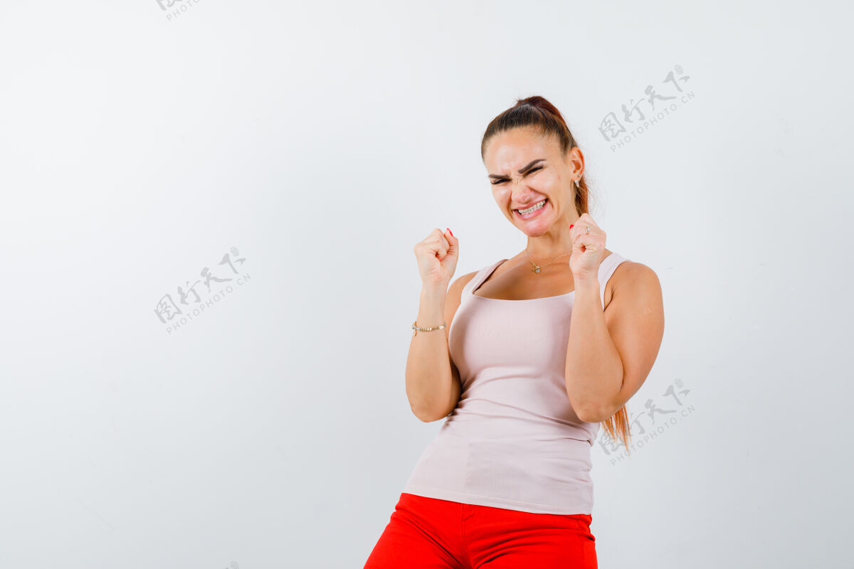 手势穿着米色上衣和红色裤子的年轻女孩展示着赢家的姿态 看上去很快乐人微笑快乐