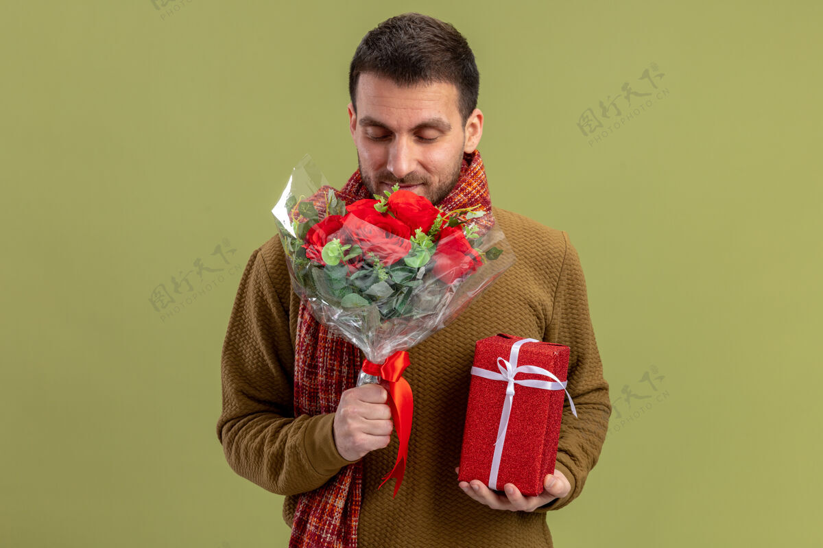 年轻身穿休闲服 脖子上围着围巾的年轻人手持一束红玫瑰 站在绿色的背景上 向大家展示快乐而积极的情人节理念玫瑰围巾男人