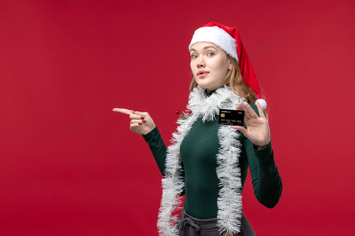 圣诞节正面图漂亮的女人拿着红色背景的黑色银行卡人物视图红色