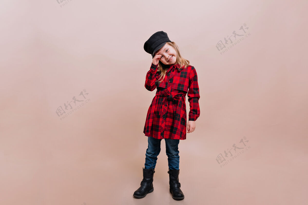 肖像可爱的小女孩穿着格子衬衫 牛仔裤和时髦的帽子 在与世隔绝的墙上摆出真正快乐的姿势欢呼女孩孩子