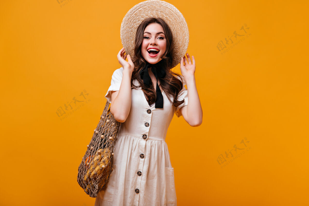 手提包一个穿着棉衣的可爱女孩拿着一个带水果的线袋子摆姿势一个戴着草帽 打着蝴蝶结的女人在橙色的背景下笑着化妆品姿势脸