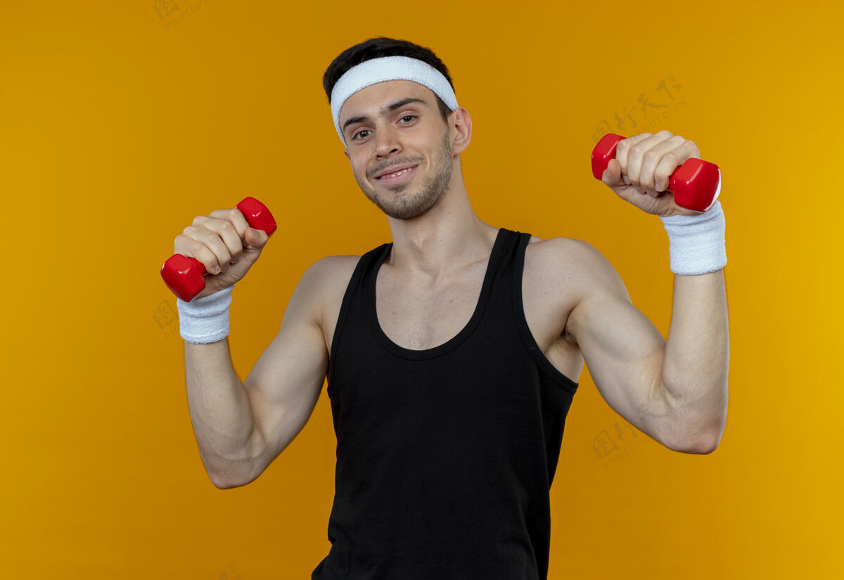 哑铃戴着头巾的年轻运动型男子 带着哑铃在橘子上微笑着锻炼身体头带站着运动