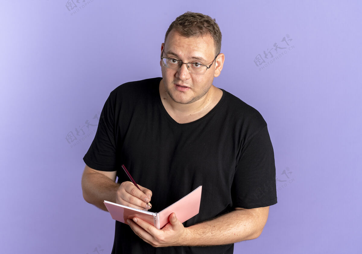 脸一个戴眼镜的超重男人穿着黑色t恤拿着笔记本 脸上带着严肃的表情写着什么眼镜男人严重