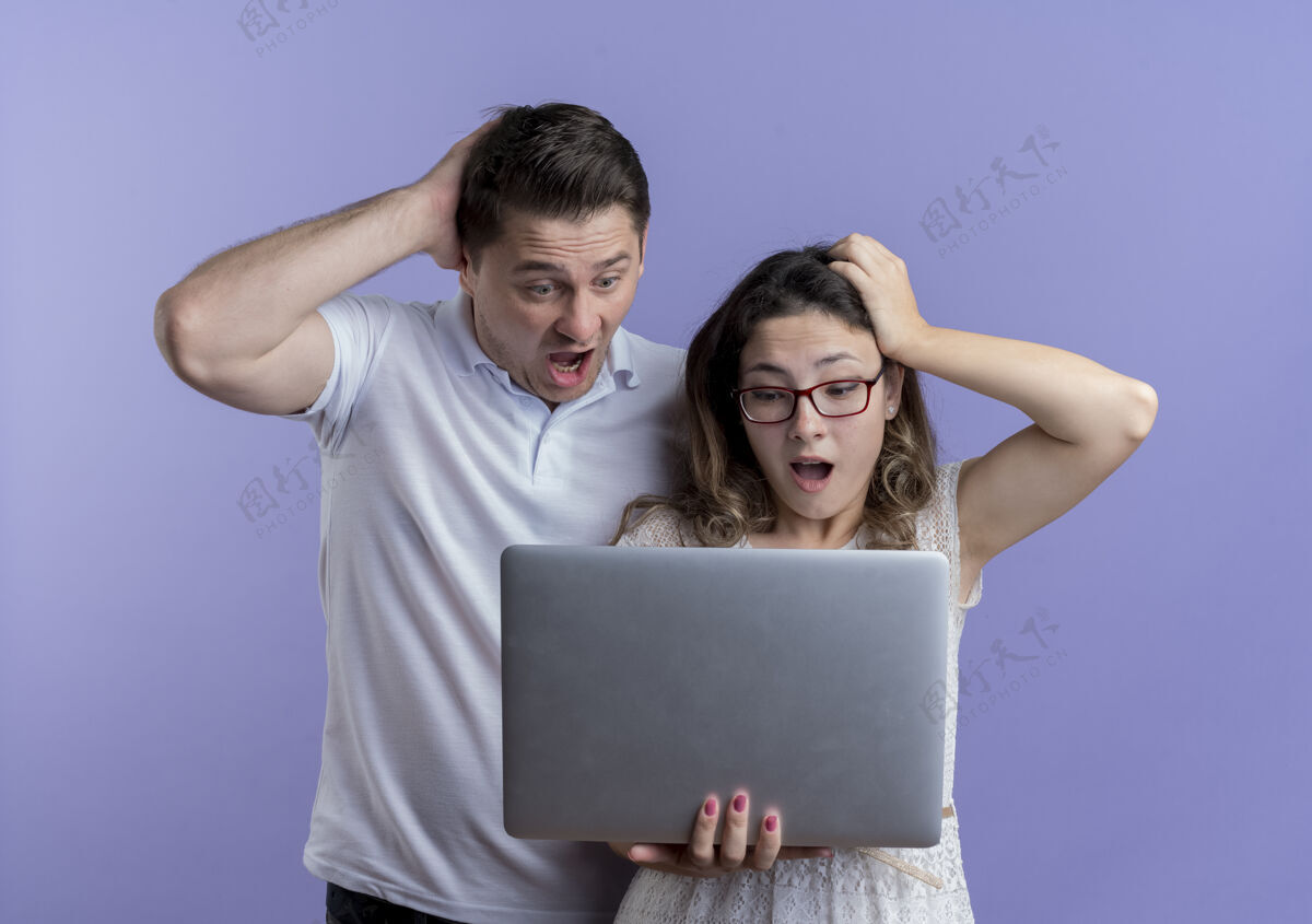 抱着一对年轻夫妇拿着笔记本电脑看着它迷惑不解 惊讶不已困惑笔记本电脑站着