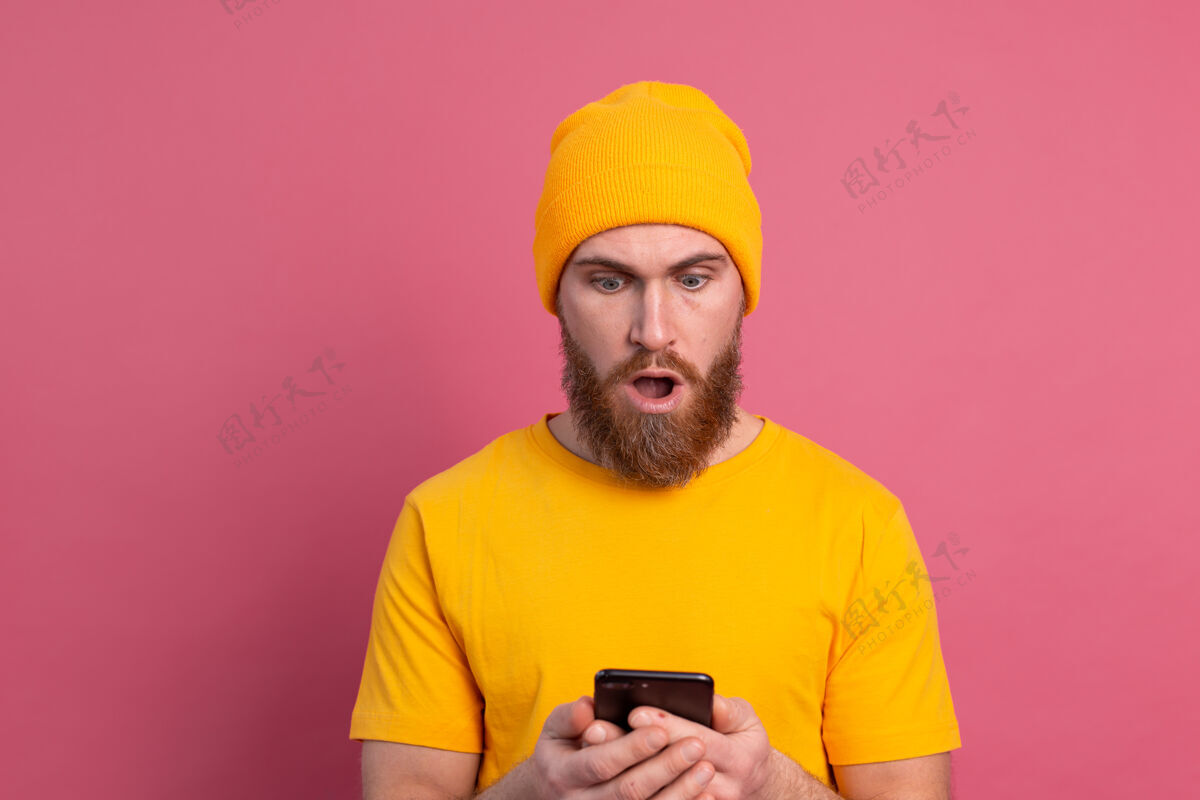 英俊照片中的关切震惊了成熟的胡须男性喘息不高兴地拿着智能手机阅读奇怪和令人不安的信息粉红色压力时尚使用