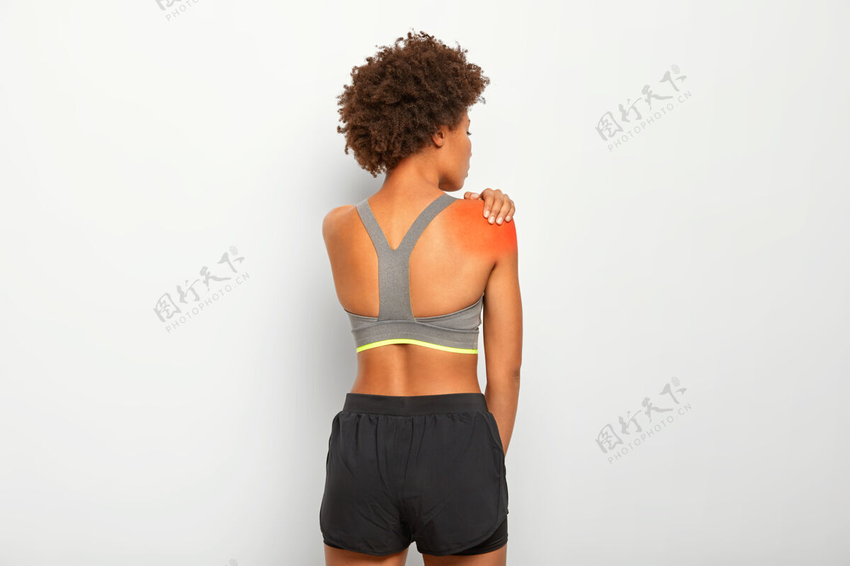 短裤苗条的女人摸肩膀 站在后面 在锻炼中受伤 穿上衣和短裤触摸背部衣服