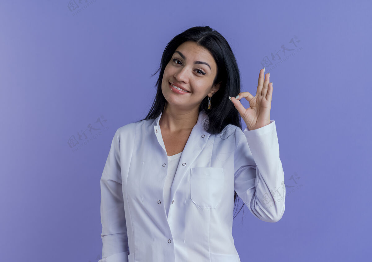 长相面带微笑的年轻女医生穿着医用长袍看着做得还好的标志微笑女人紫色