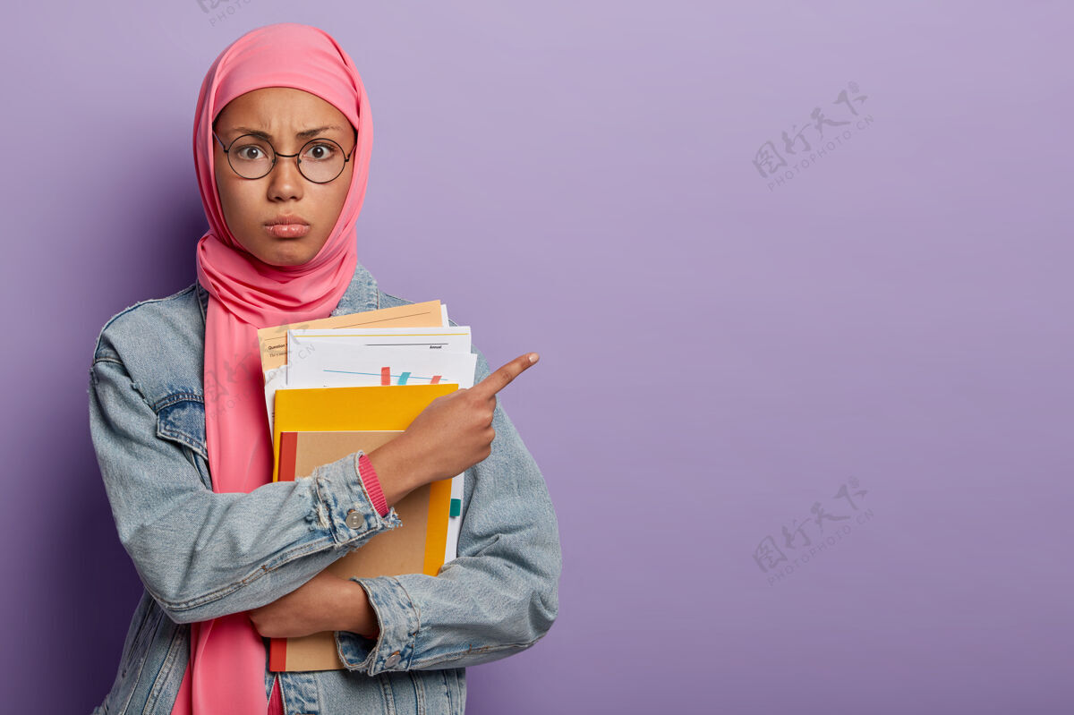 眼镜十几岁的女学生拿着纸和课本摆姿势 在空闲的地方站在一边 戴着圆眼镜和粉色头巾教育消极
