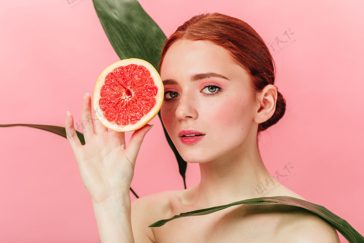 裸体灵感女孩摆出绿叶和柑橘的姿势工作室拍摄的姜汁女人站在粉红色背景上的葡萄柚葡萄柚年轻人女孩