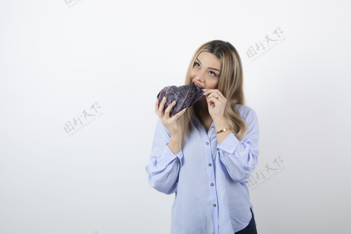 金发穿蓝色衣服的漂亮女人在吃白色背景上的紫色卷心菜女人模特吃