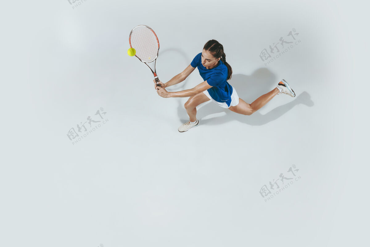 比赛穿蓝色球衣打网球的年轻女子她用球拍击球室内击球与白色隔离年轻 灵活 力量和活力负空间顶视图私人教练球快乐