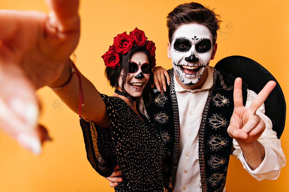 文化一对穿着万圣节服装的情侣在自拍身着墨西哥服装的微笑女士和男友一起庆祝死亡日骷髅帽子万圣节
