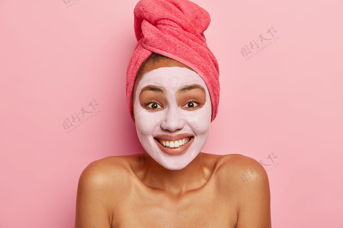 无忧无虑快乐女人画像应用粘土滋养面膜 有愉快的表情 心情好 享受青春的治疗 在湿头发上戴玫瑰红的毛巾乐观眼睛室内