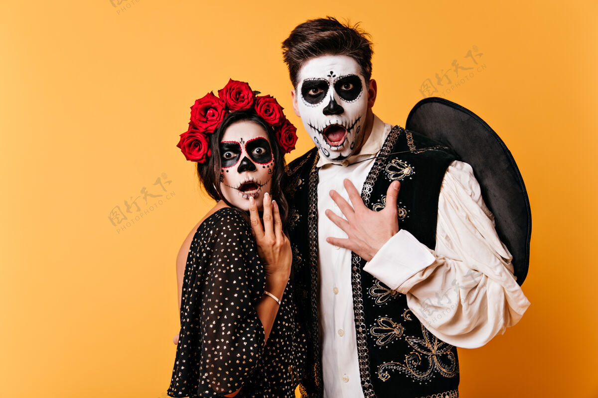 骷髅万圣节彩绘脸的男孩和女孩惊呆了在隔离墙上拍摄了一对身着墨西哥民族服装的夫妇恐怖男人花
