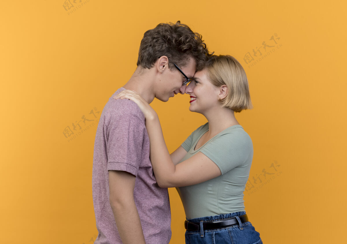 拥抱一对年轻漂亮的情侣穿着休闲服站在一起 在爱中幸福地拥抱在橙色的墙上衣服情侣男人