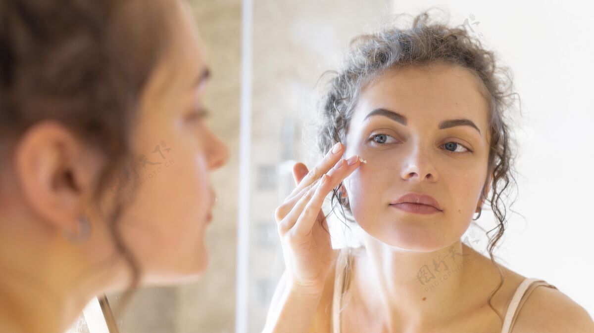 模特女人照镜子在脸上涂面霜美容面部护理镜子