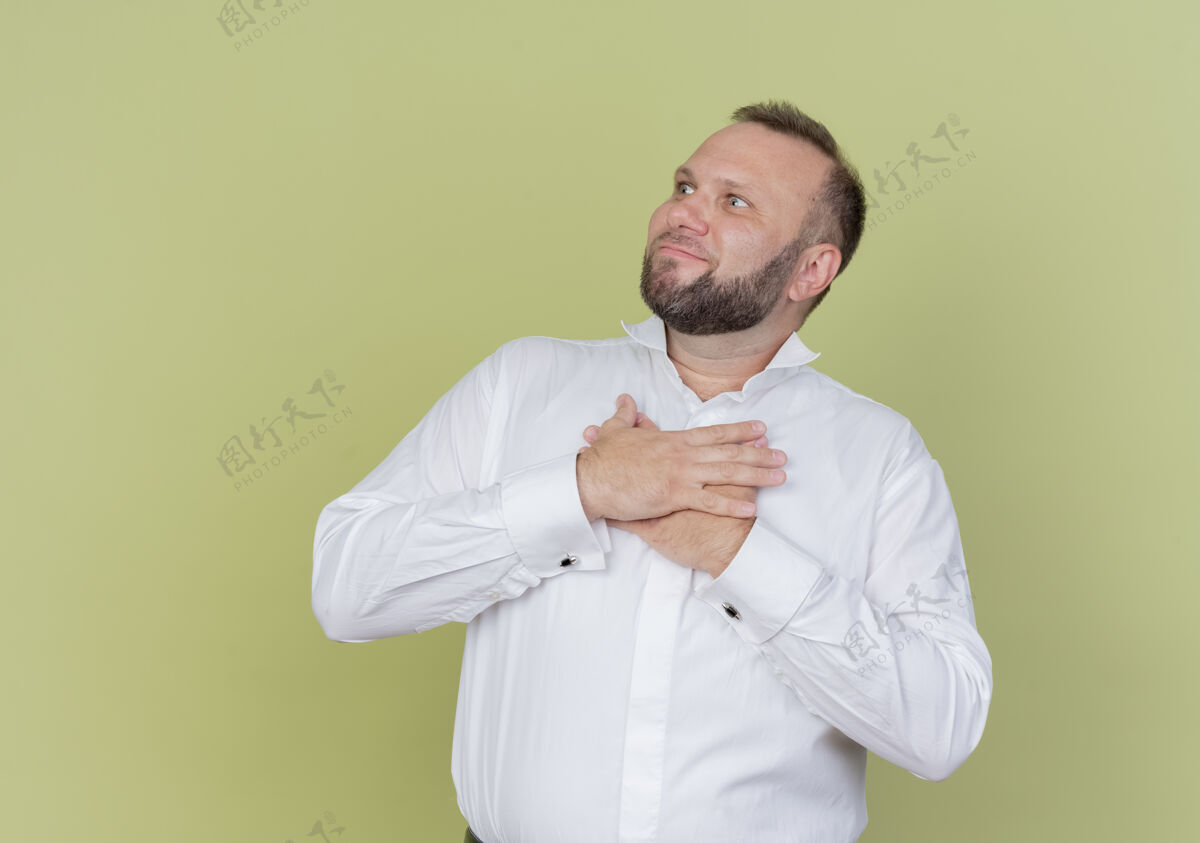 胸一个留着胡子的男人穿着白衬衫 一边看着一边 手放在胸前 站在光墙边 心怀感激站胡子放一边