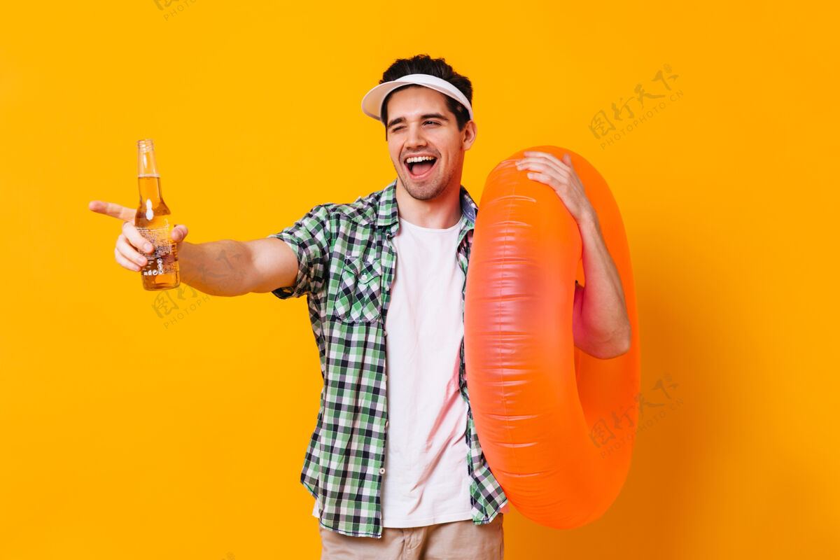 短裤风情万种的调情男人拿着一瓶啤酒和充气橘子圈眨眼摆姿势衣服文件水果