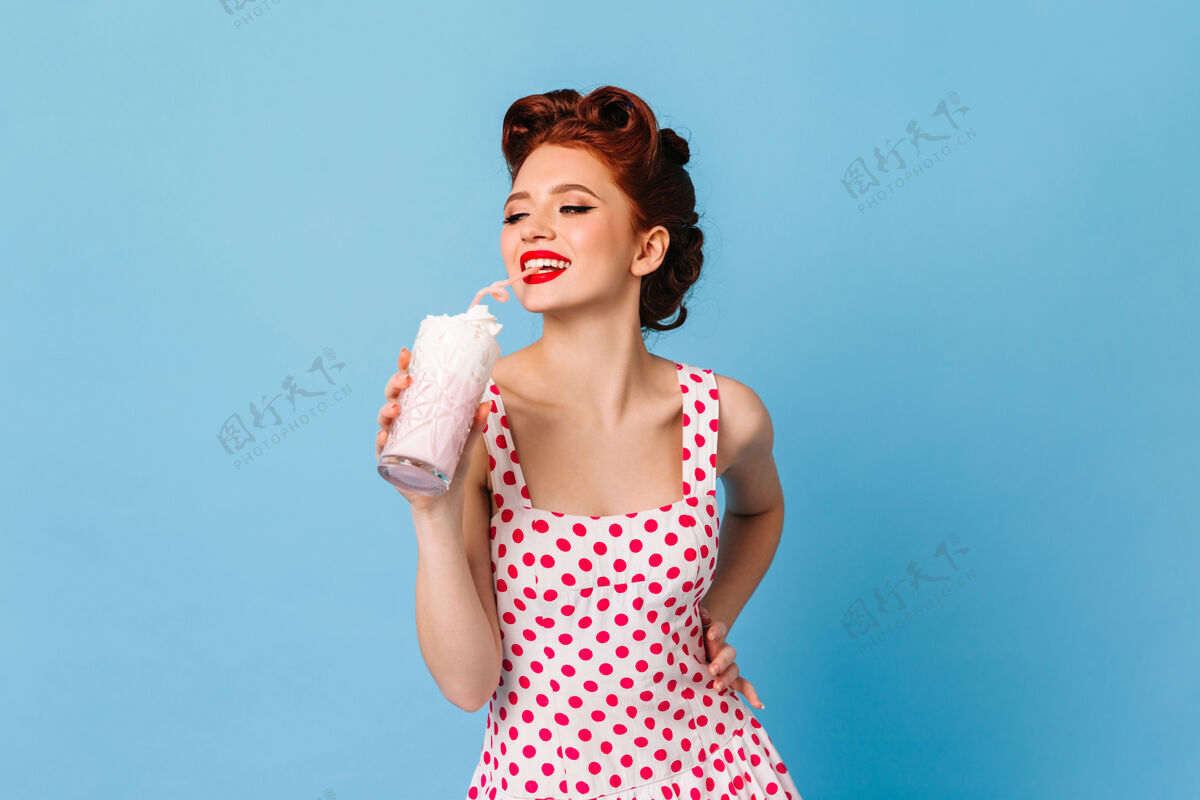 欧式灵感女孩在波尔卡圆点连衣裙喝奶昔笑姜女模特举行饮料在蓝色空间奶昔蓝色隔离时尚