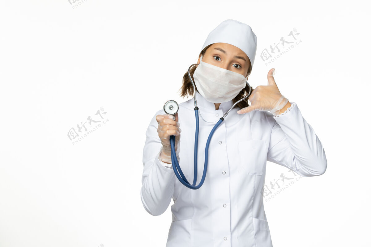 大流行正面图女医生穿着白色医疗服 戴着口罩 在白色办公桌上用听诊器进行大流行性疾病药物病毒隔离前台医生使用