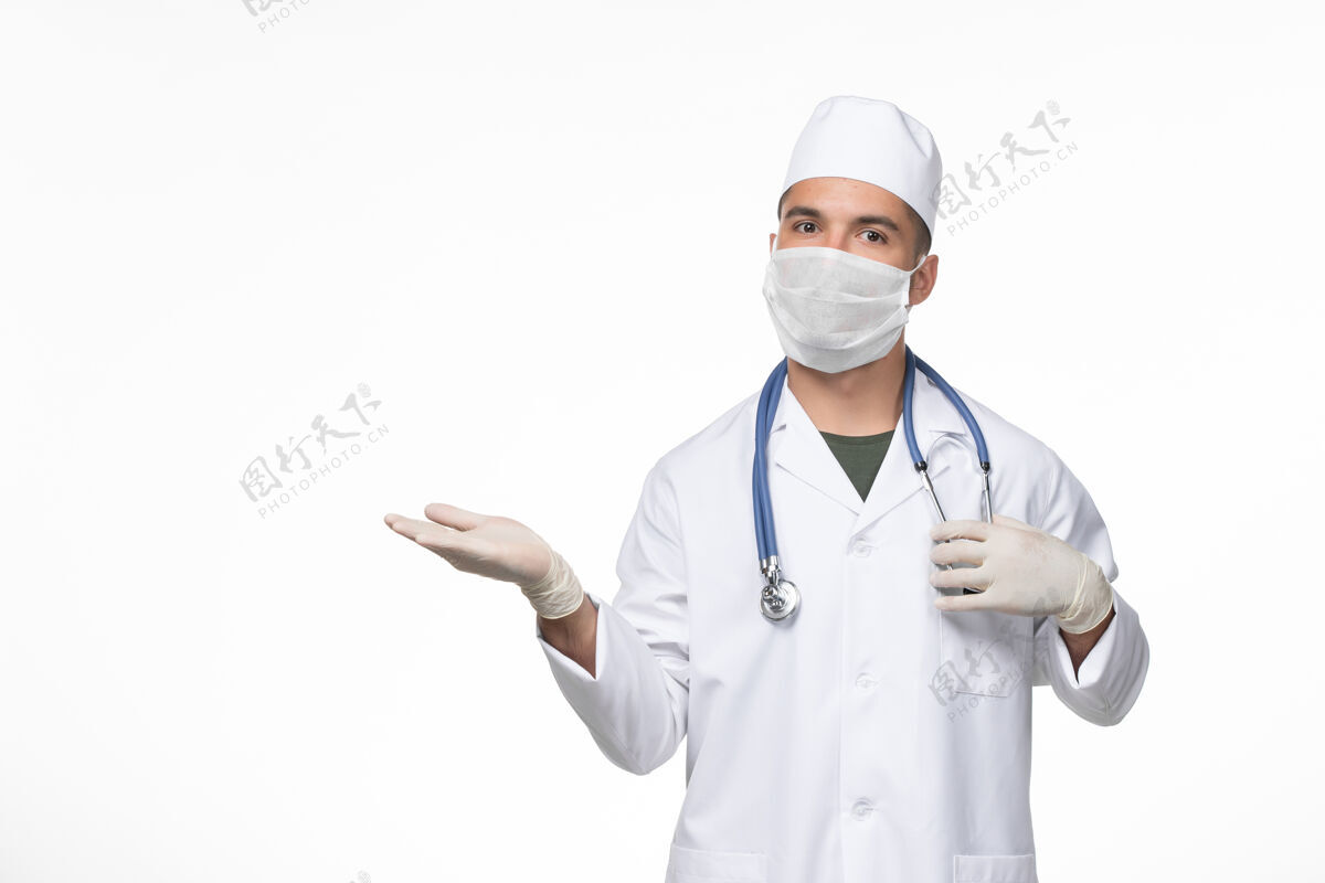 疾病正面图：男医生穿着医疗服 戴着口罩 在白色桌面上用听诊器抵御冠状病毒-病毒疾病大流行办公桌男性医疗