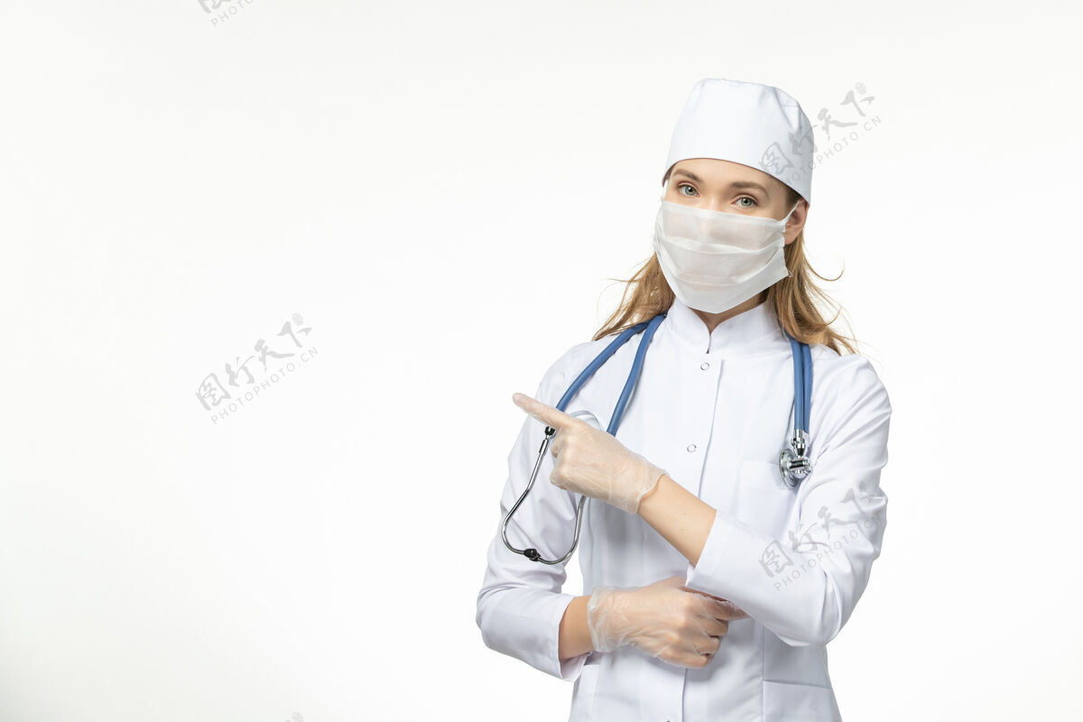 面罩正面图女医生身穿白色医疗服 带无菌口罩 因白墙上冠状病毒病大流行疾病冠状病毒-女性医生听诊器