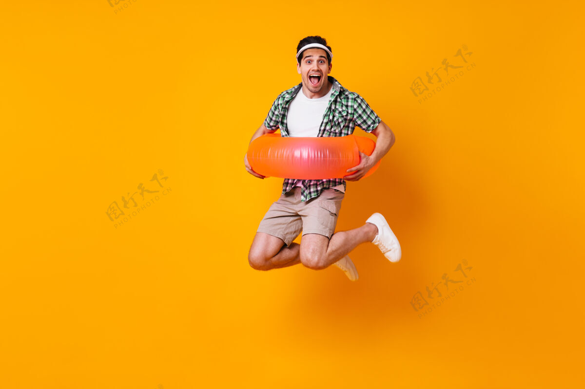 正面穿着短裤和衬衫的活泼男人穿上充气圈 跳上橙色的空间冒险带背包