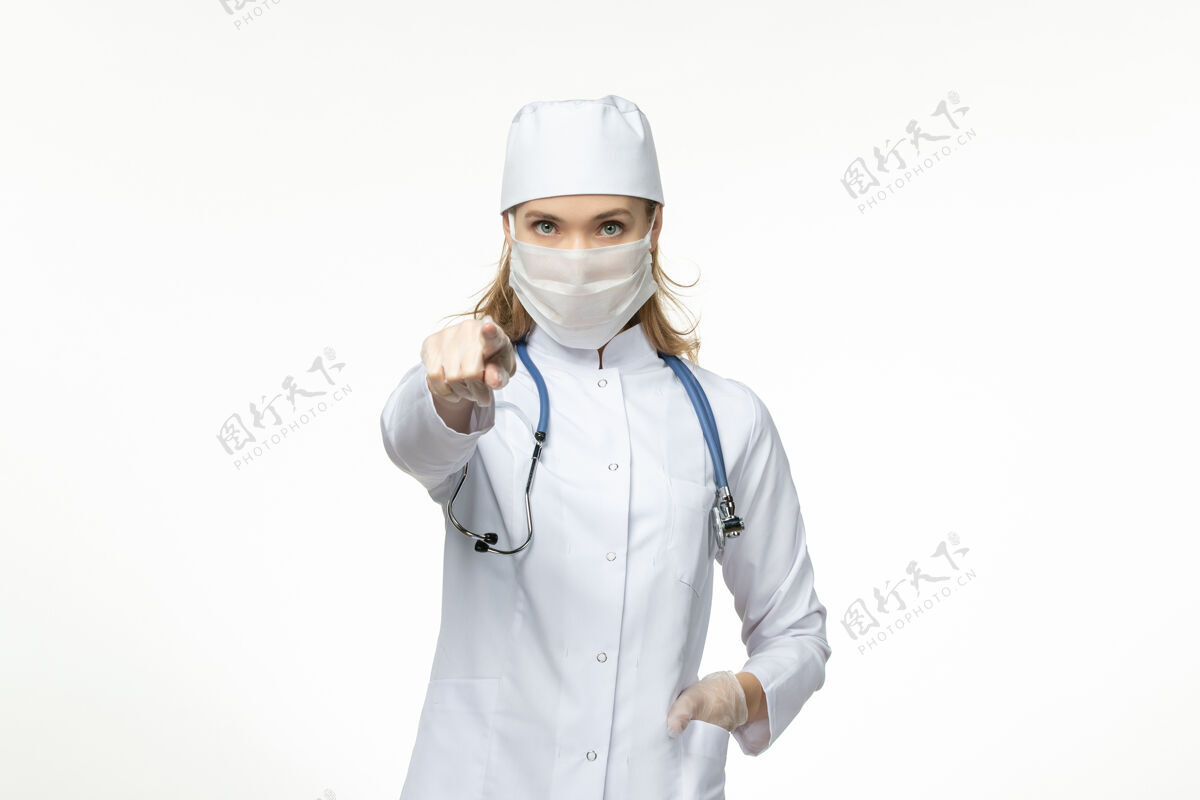 套装正面图女医生穿着医疗服戴着口罩和手套因冠状病毒在浅白的办公桌上大流行冠状病毒病到期听诊器手套