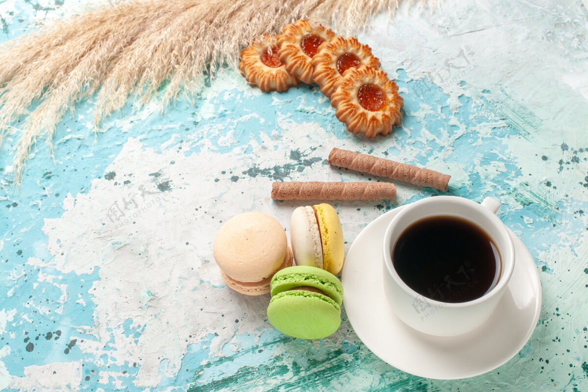 咖啡因前视图一杯茶 蓝色表面上有饼干和麦卡龙蛋糕 甜甜的双份糖馅饼早餐麦卡龙生的
