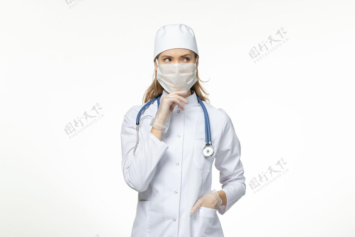 口罩正面图女医生身穿医疗服戴口罩因冠状病毒思考白墙病冠状病毒-大流行性病毒病护士医疗女性