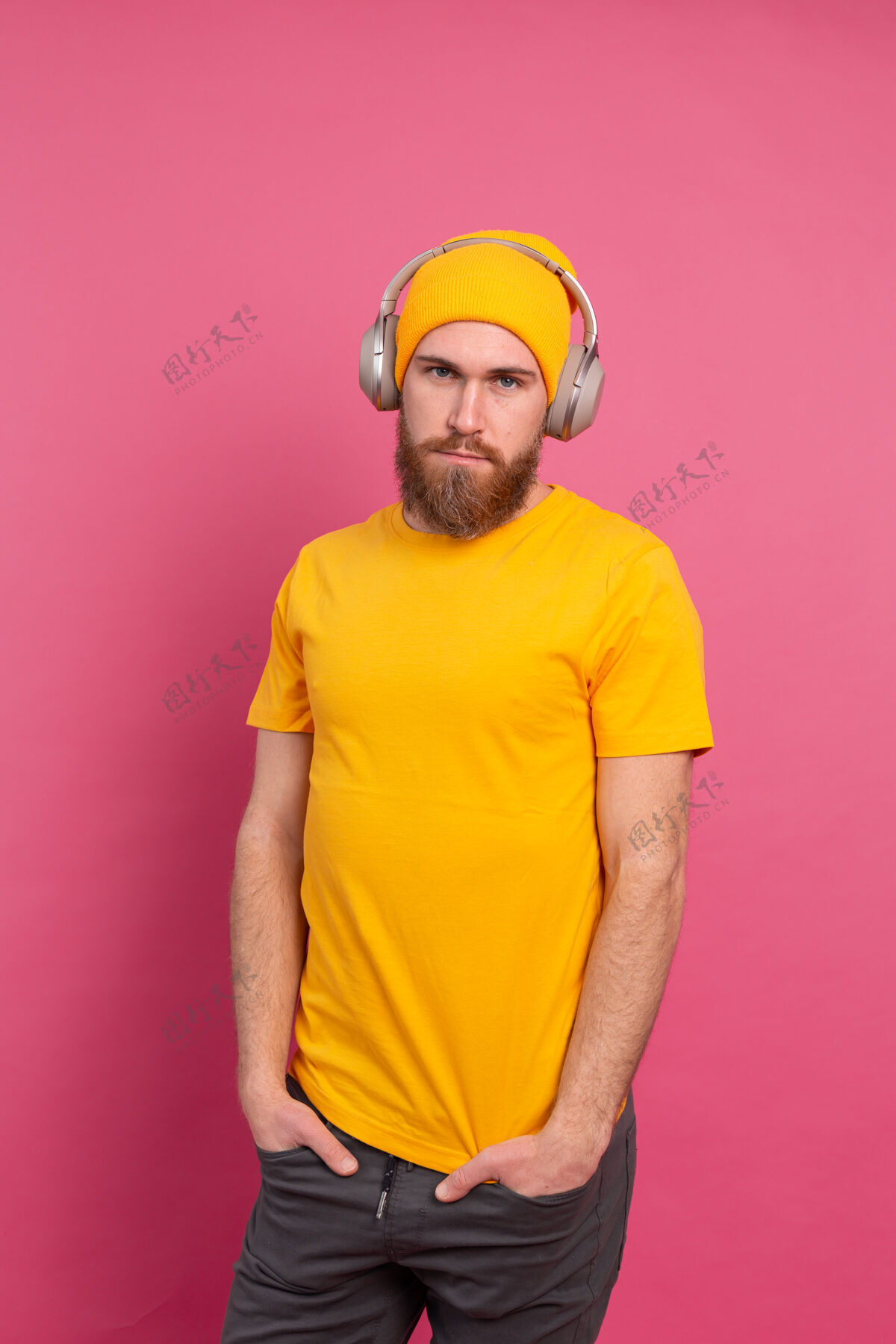 微笑帅哥在随意地听着音乐 用耳机隔离在粉色背景上休闲成人男性