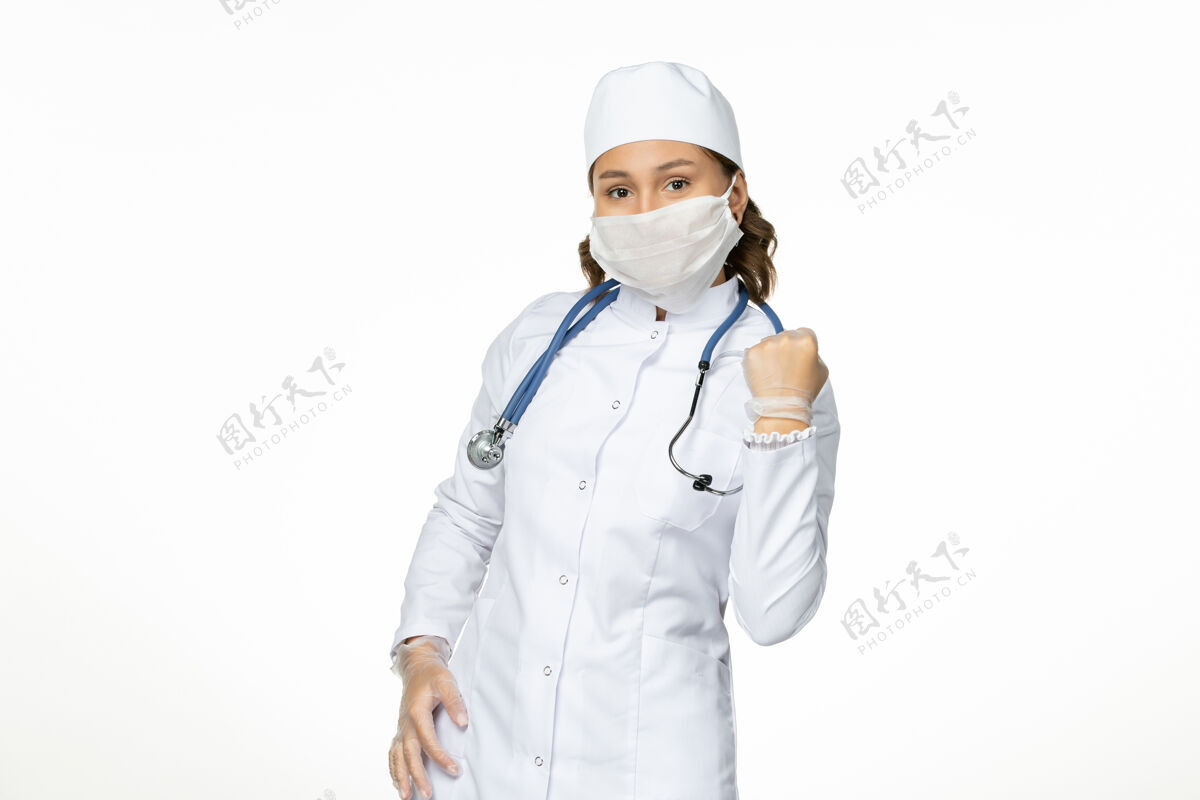 女性正面图女医生身穿白色医疗服 戴着口罩因冠状病毒欣喜于白墙大流行性疾病隔离冠状病毒正面套装冠状病毒