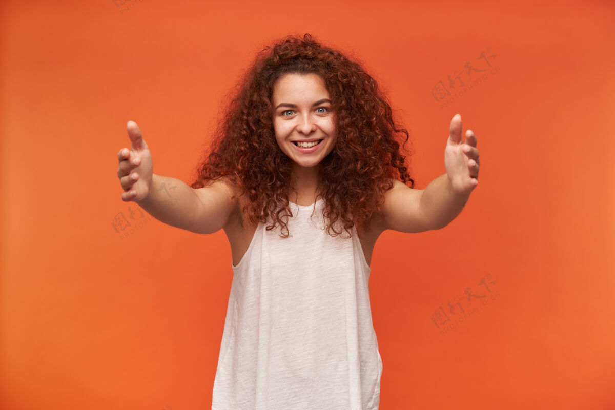 拥抱迷人可爱的红头发卷发女孩的画像穿着白色露肩上衣张开双臂 试图拥抱你孤立在橙色的墙上面部20多岁微笑