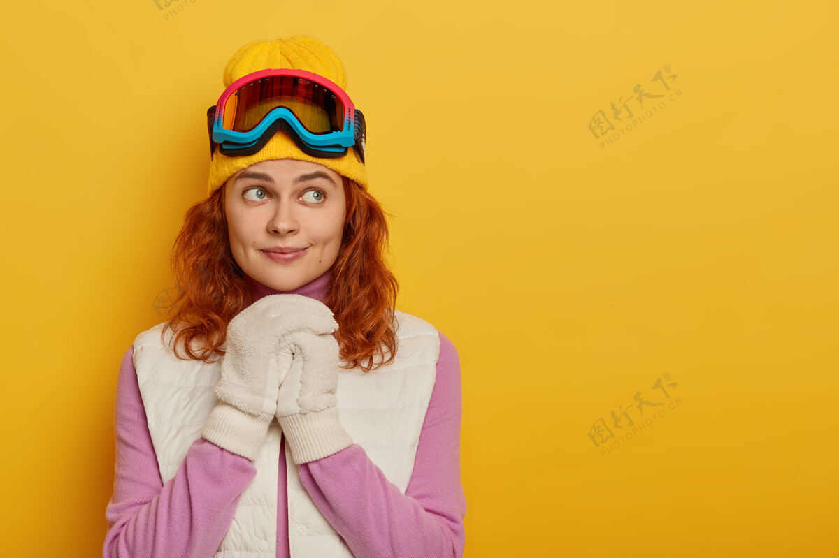 运动装沉思的红发女游客的照片享受滑雪板 站在黄色的背景下 戴着白色手套和滑雪护目镜文字空间手持Swoosh