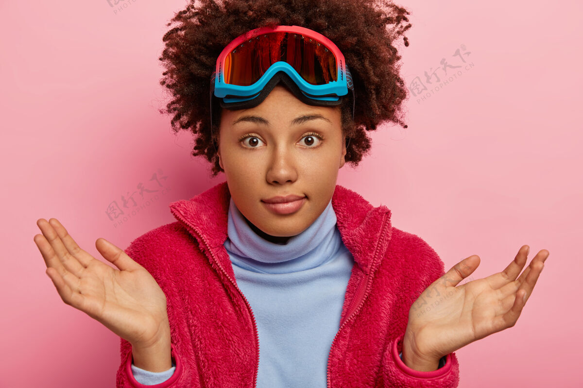 年轻无知的女性度假者 踌躇地摊开手掌 头戴滑雪面罩 休闲装 在室内摆姿势手掌一不知道