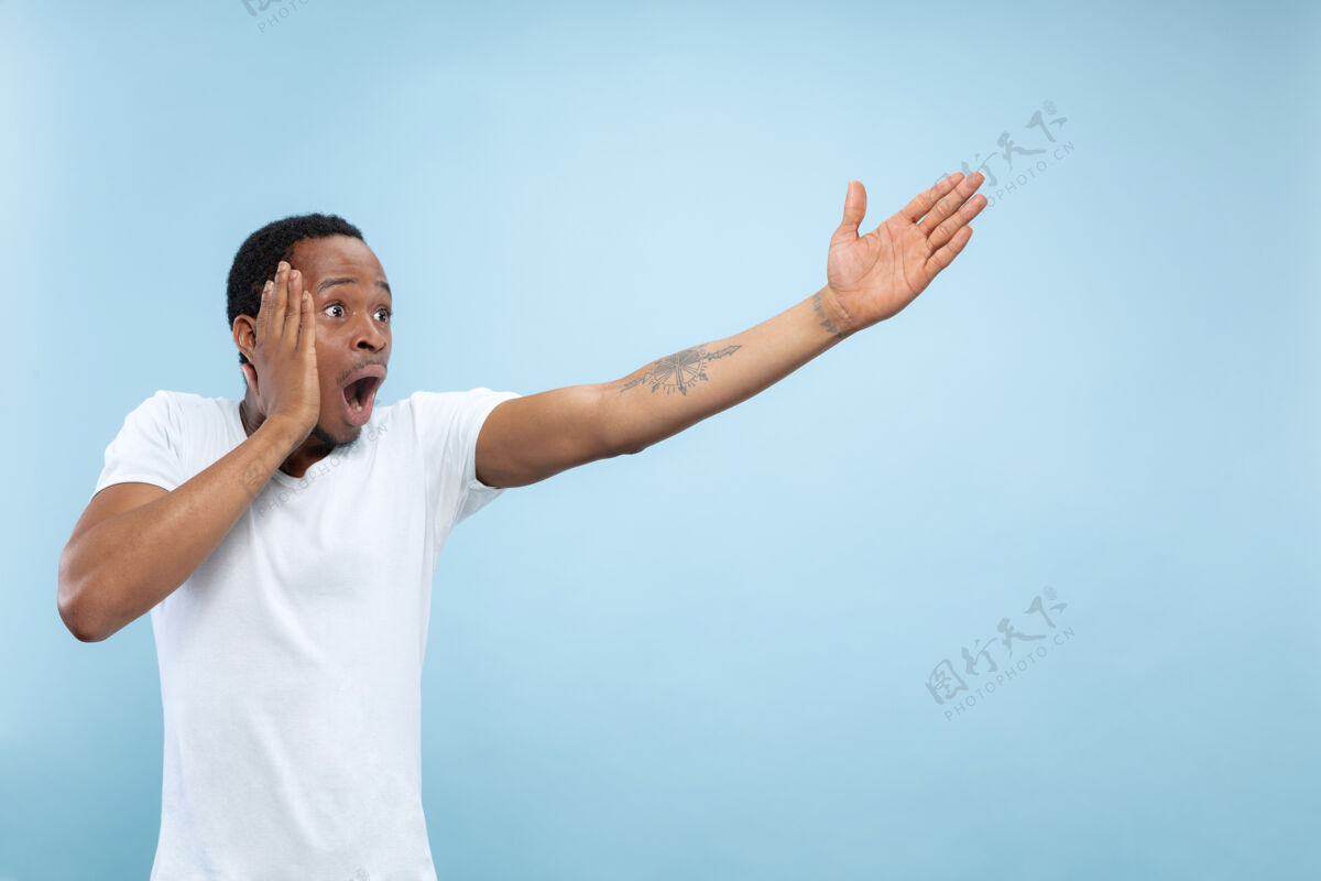 手势半身特写肖像的年轻非洲裔美国男子在白色衬衫的蓝色空间人类的情感 面部表情 广告 销售理念指向 选择 惊讶表情显示一半