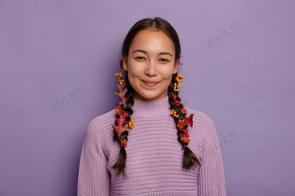 休闲快乐自然的亚洲女人庆祝秋天 有两个用红色秋叶 浆果和花朵装饰的辫子 穿着紫色毛衣 隔离在紫罗兰色的墙上十月时间微笑毛衣年轻