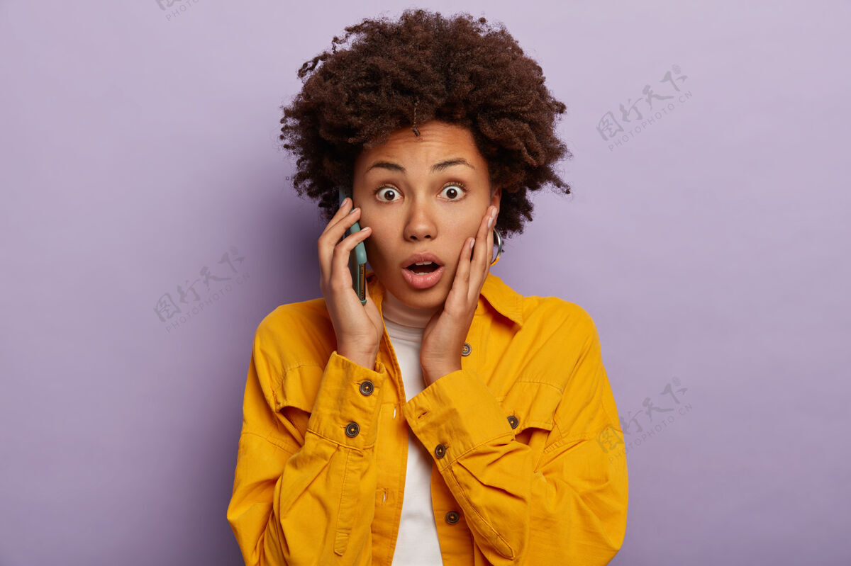 夹克漂亮的非洲女人的肖像在电话中得到惊人的消息 摸了摸脸颊 穿了一件鲜艳的犹太夹克 睁开眼睛张嘴听到惊人的变化站在室内拿着紫色表情