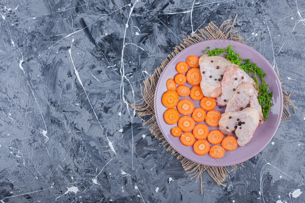 蔬菜把切成片的胡萝卜 鸡翅和青菜放在盘子里 放在蓝色表面的粗麻布上新鲜蛋白质盘子