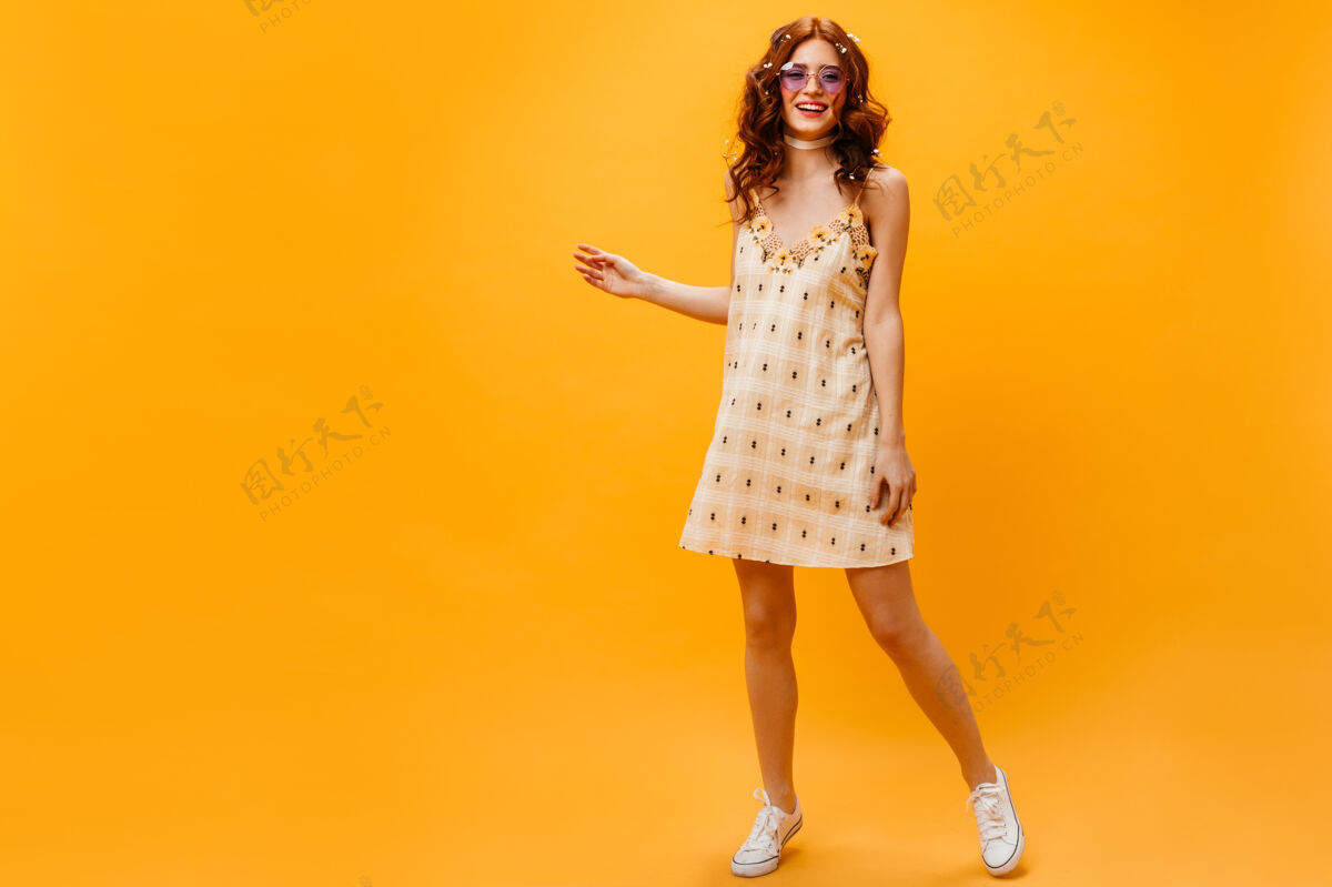 微笑一个穿着黄色短裙 身材苗条的年轻女子一个戴着墨镜的红发女子在橙色背景下摆姿势优雅华丽发型