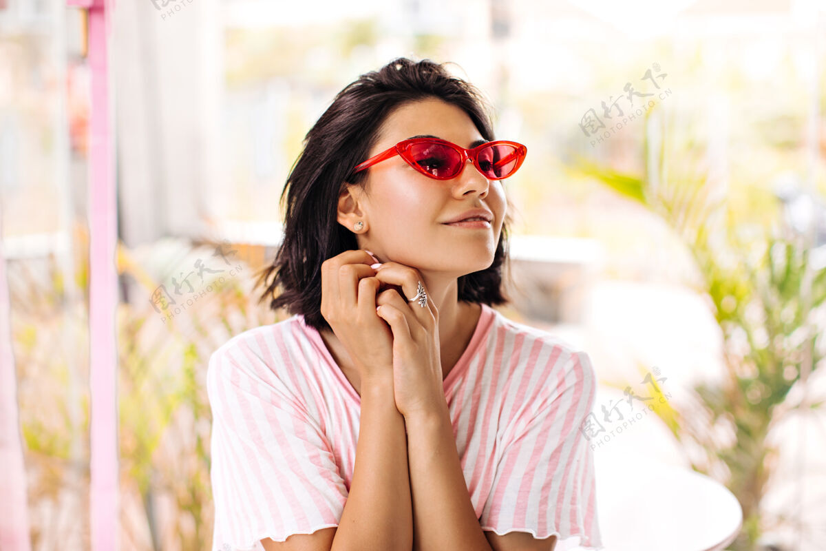 享受梦幻般的时尚女士 戴着戒指 在模糊的背景上遥望远方夏季 灵感来自深肤色 戴着粉色太阳镜的女士的户外照片表情发型配饰