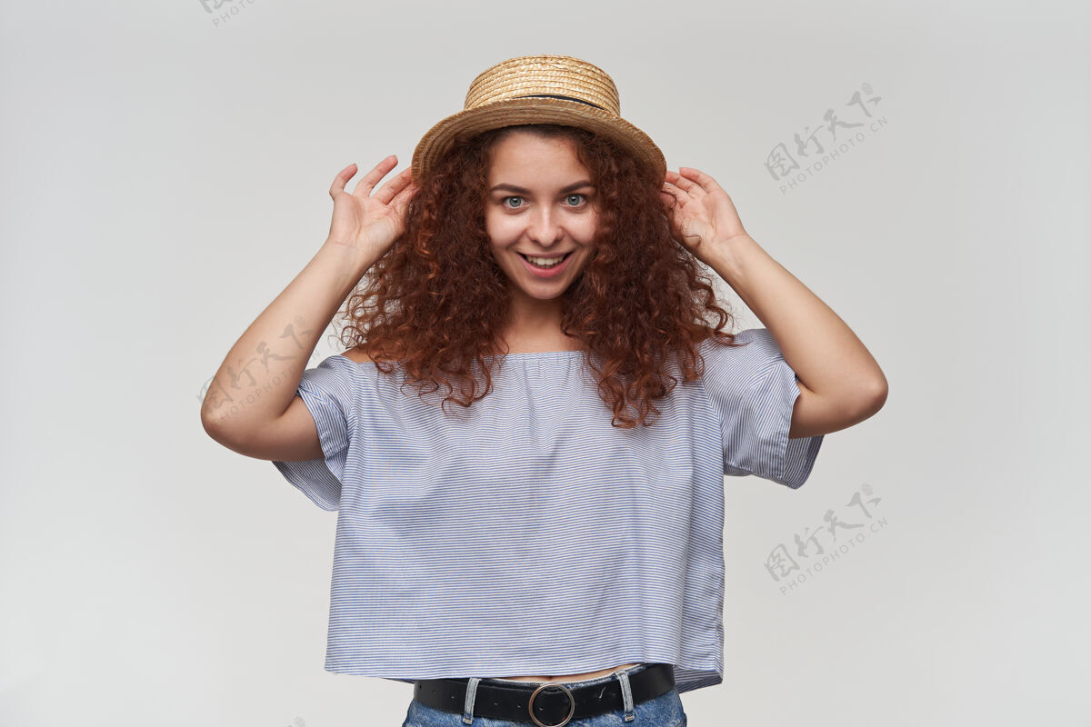 青少年有魅力的成年红头发女孩的肖像 卷发穿着条纹露肩上衣和帽子触摸她的帽子和微笑隔着白色的墙壁孤立微笑皮肤20多岁
