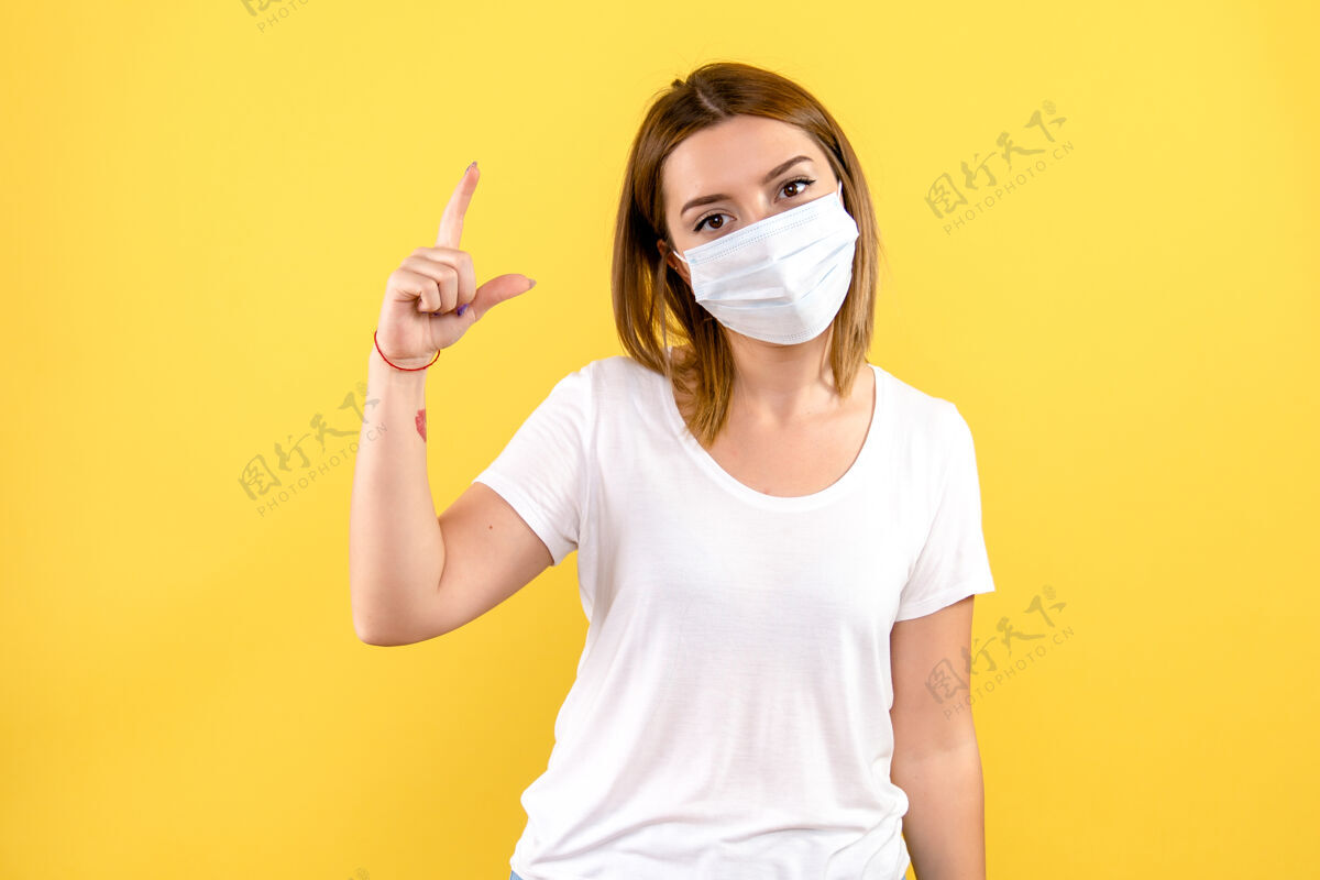 病毒黄色墙壁上戴着无菌口罩的年轻女子的正视图护士年轻女性健康