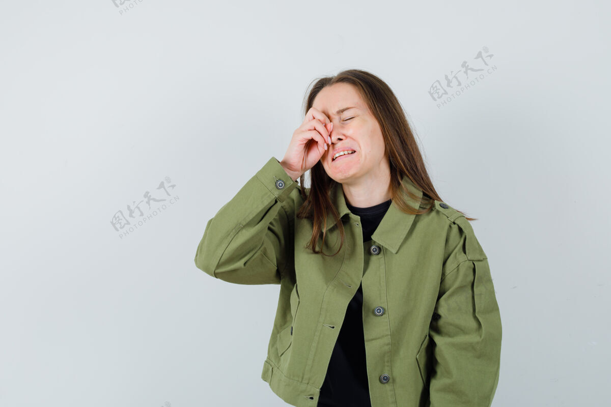 休闲身穿绿色夹克的年轻女子一边哭一边揉着眼睛 表情悲伤 正对着前方看女人时尚时尚